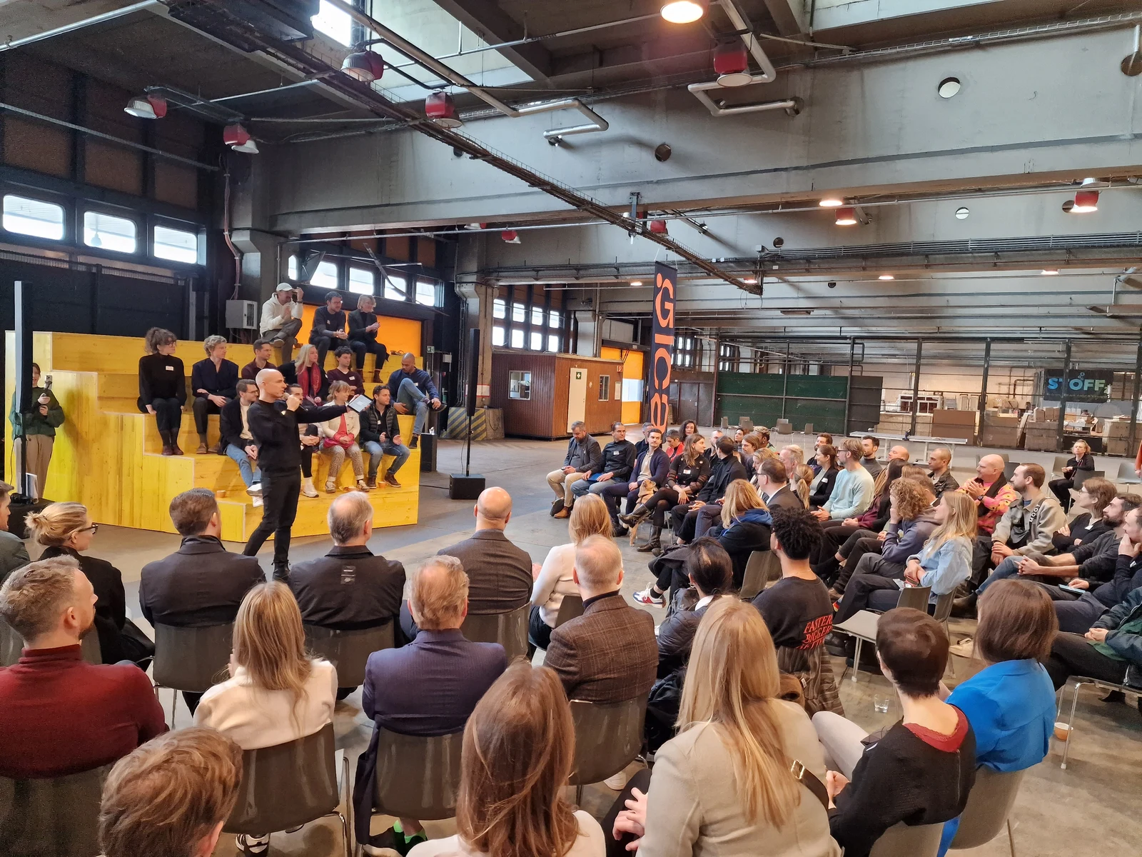 Große Gesprächsrunde mit einem Sprecher in einer offenen Berliner Industriehalle